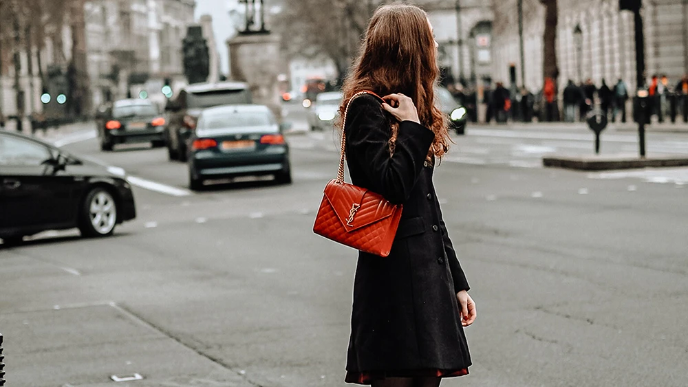 Femme habillée en noir dans un centre-ville tenant un sac à main rouge